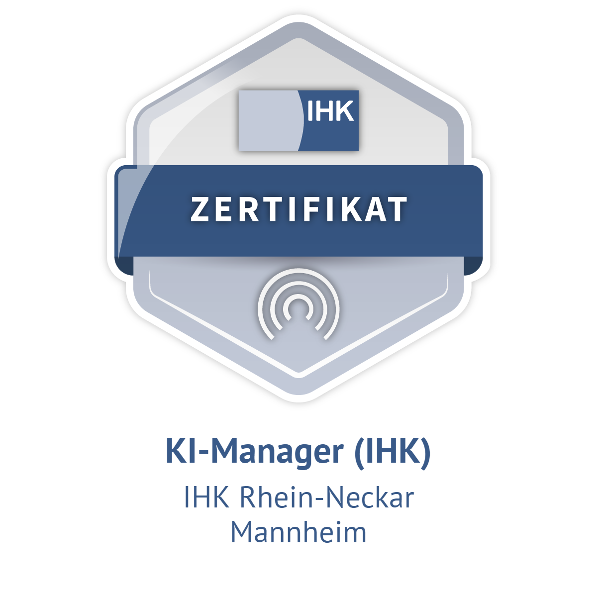 A digital badge or certificate icon for a "KI-Manager (IHK)" (AI Manager (CCI)) certification offered by IHK Rhein-Neckar in Mannheim. The badge is a stylized hexagon with a smaller inner hexagon. The top section features a light gray rectangle with the acronym "IHK" in dark blue. A dark blue banner across the middle prominently displays the German word "ZERTIFIKAT" (CERTIFICATE) in white. The lower section contains a light gray circular design with concentric arcs, the text "KI-Manager (IHK).